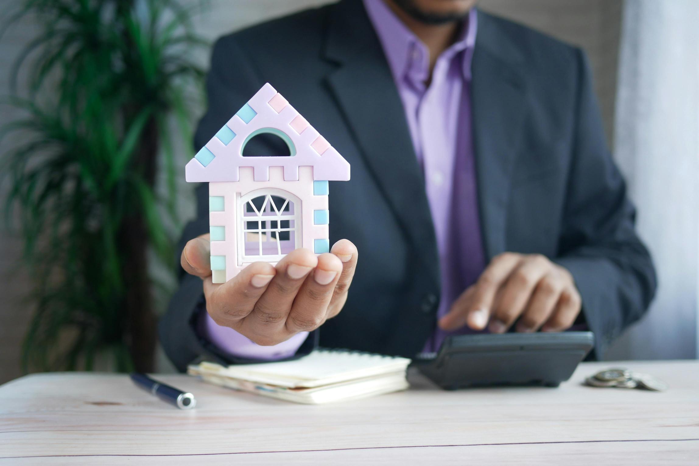 An estate agent in a suit holding a small model of a house