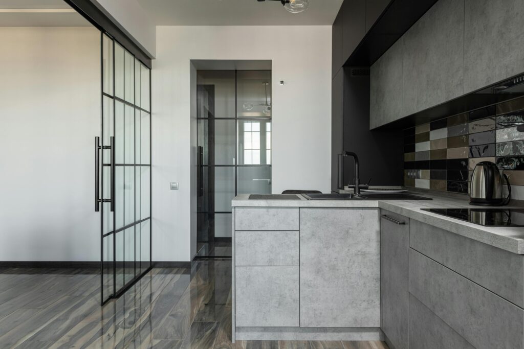 A grey concrete-effect kitchen with grey floor and steel framed doors onto a lounge space