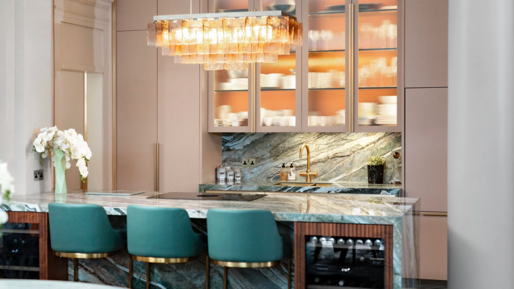 A beautiful kitchen with ceiling height pink cabinets with glass doors and statement green bar stools
