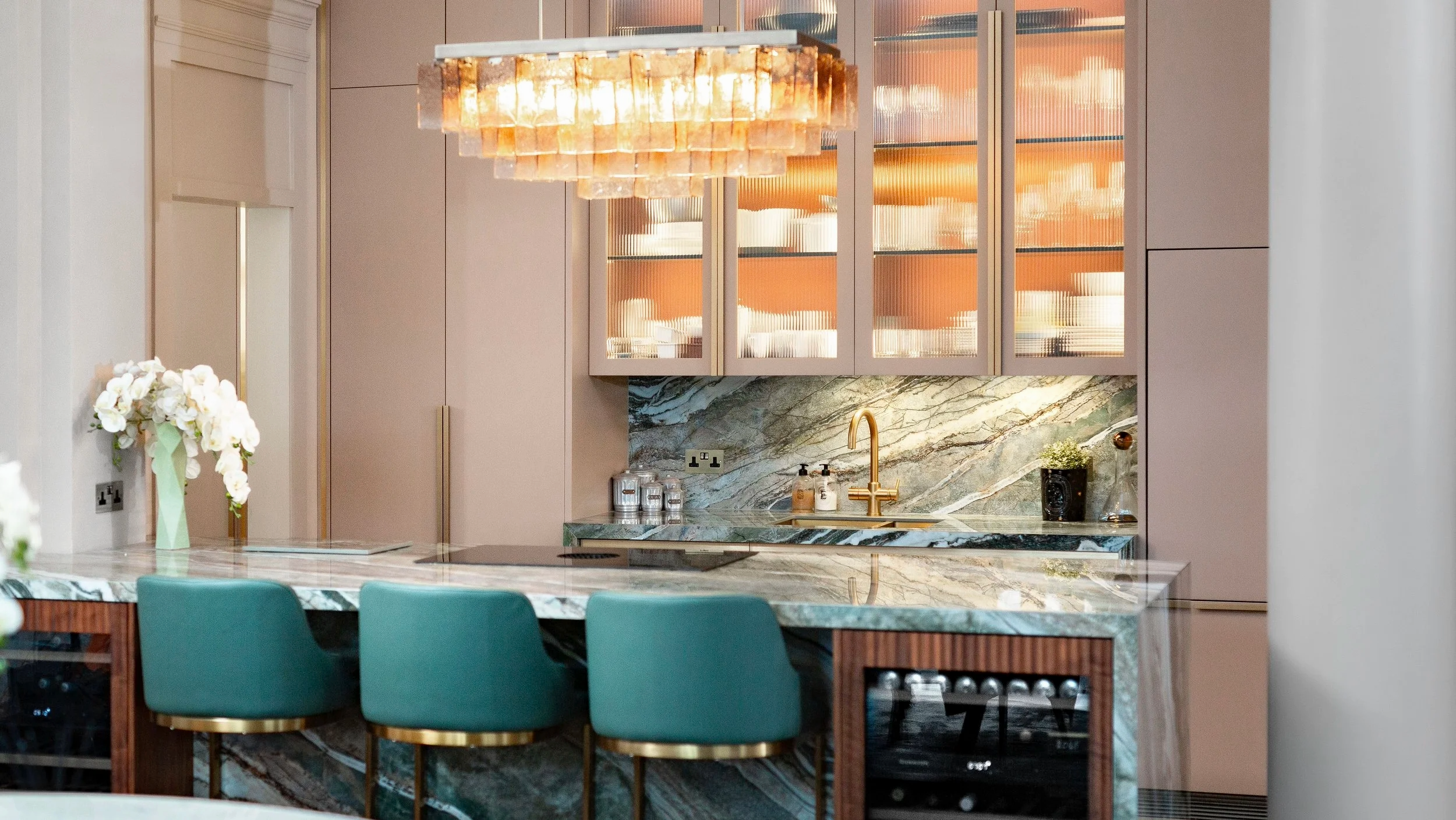 A beautiful kitchen with ceiling height pink cabinets with glass doors and statement green bar stools